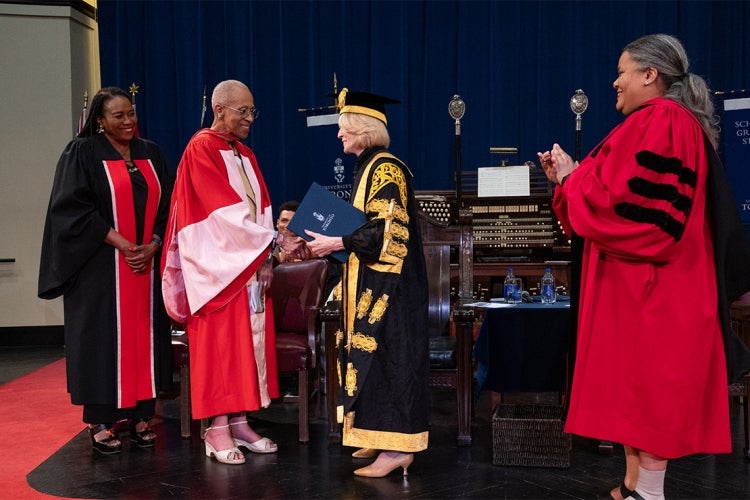 Zanana Akande on stage with Rose Patten and being hooded by Professor Ann Lopez