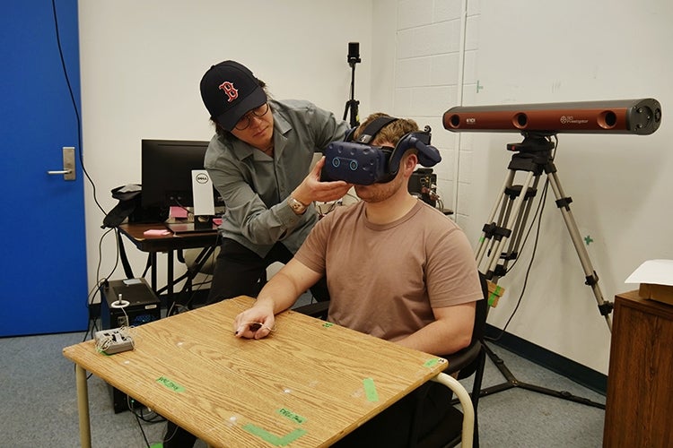Researcher adjust a VR headset that is being worn by a student