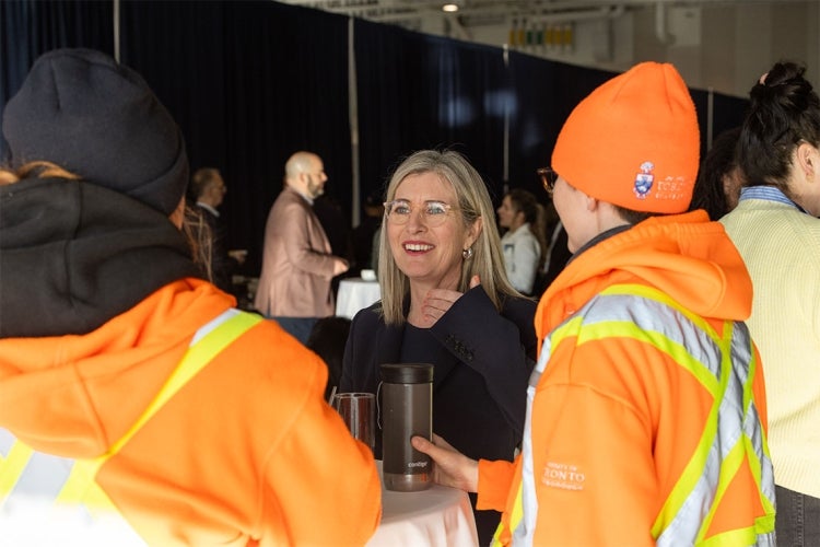 Staff members, wearing orange safety jackets, chat with Melanie Woodin