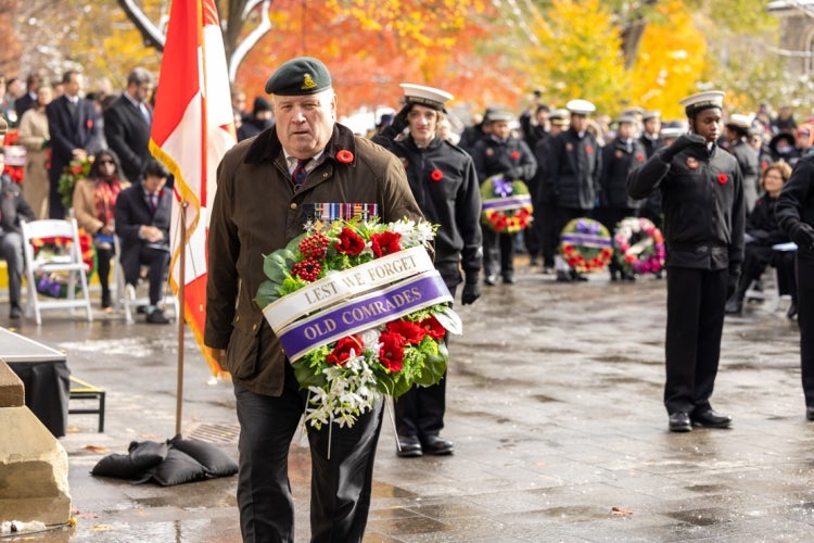 an older soldier holds a wreath that reads "lest we forget old comrades"